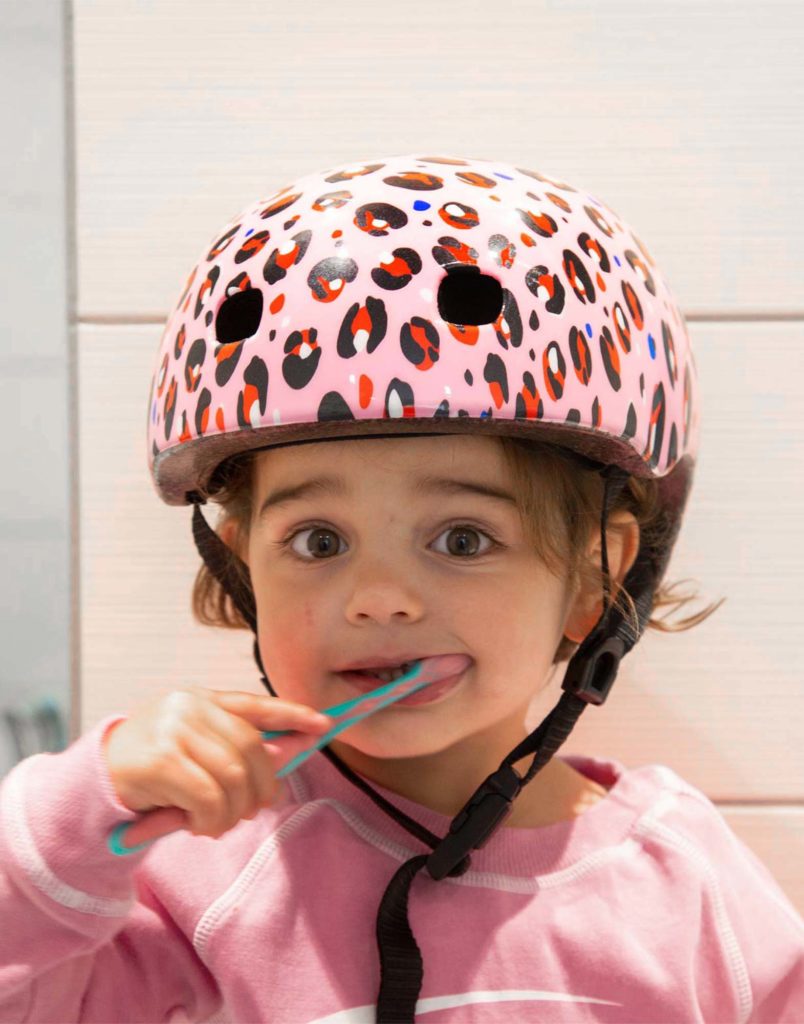 girl brushing her teeth wearing micro scooter bike leopard helmet